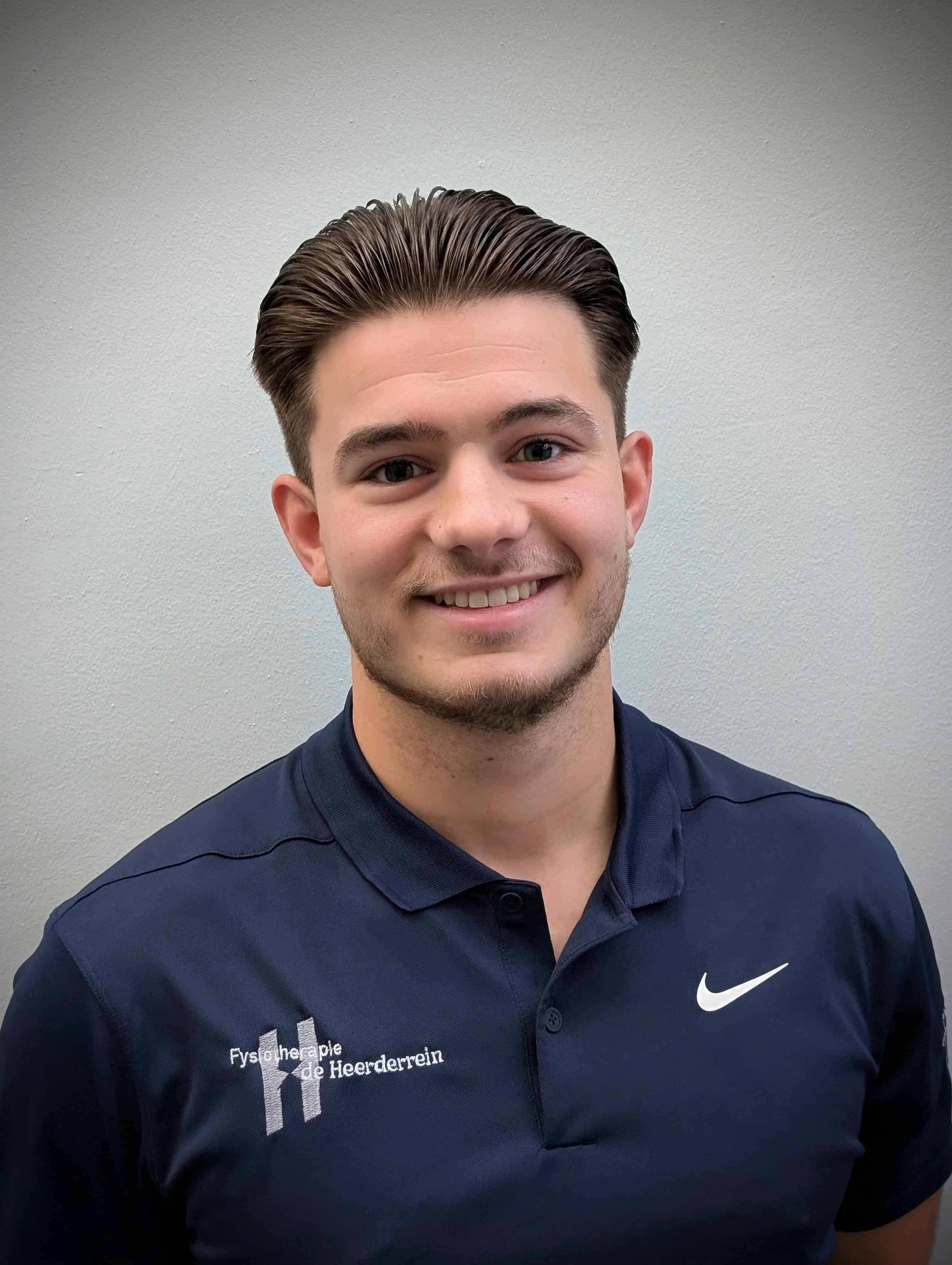 Gezicht van een jonge mannelijke fysiotherapeut met een brede glimlach voor de praktijk.